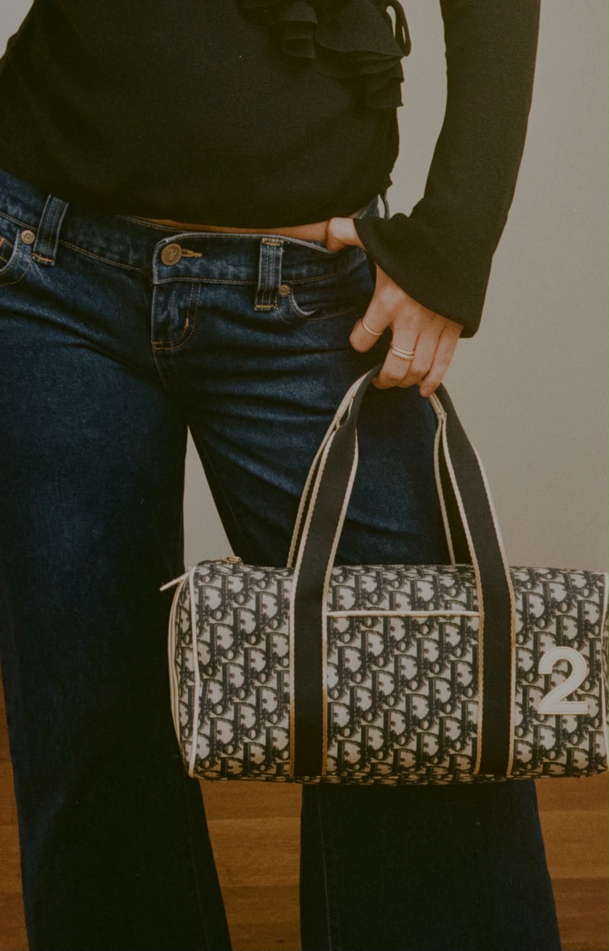 A Dior Oblique duffle bag held at the hip over dark denim