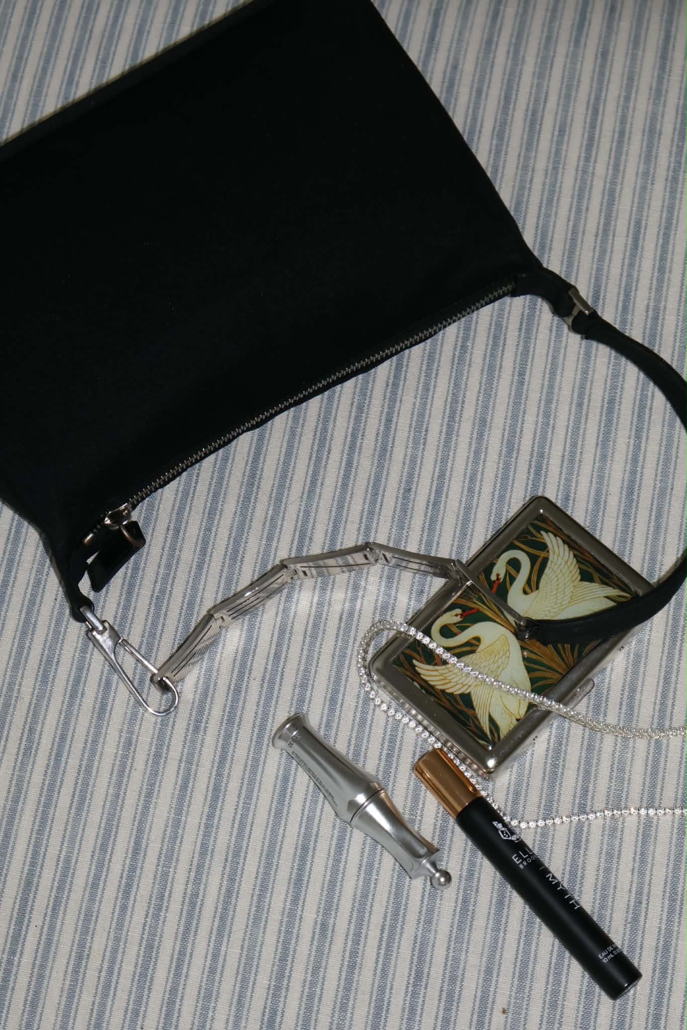 Overhead of the black bag on striped ticking with the silver chain strap looped away from it