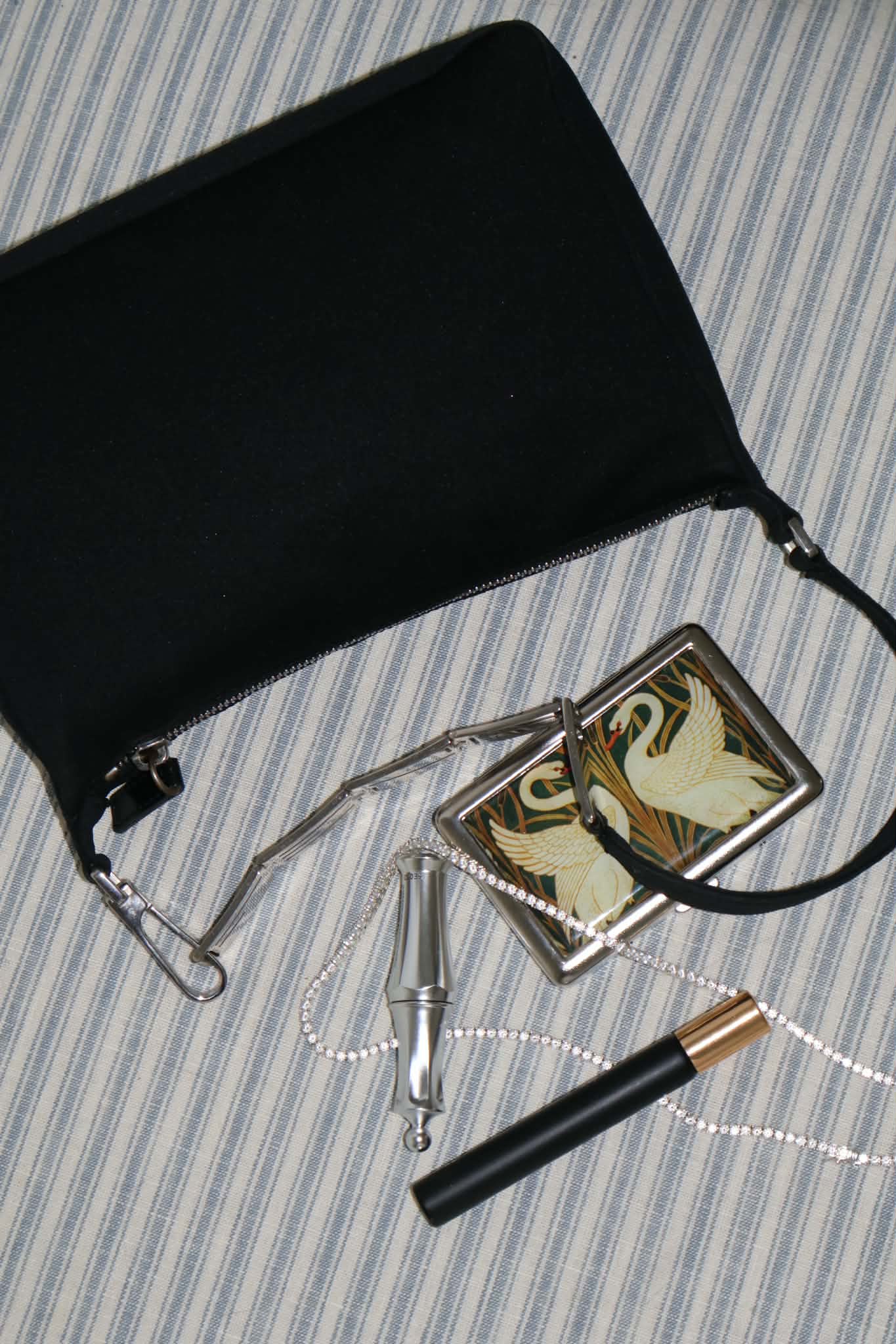 The black shoulder bag laid on blue striped ticking with its accessories fanned out below